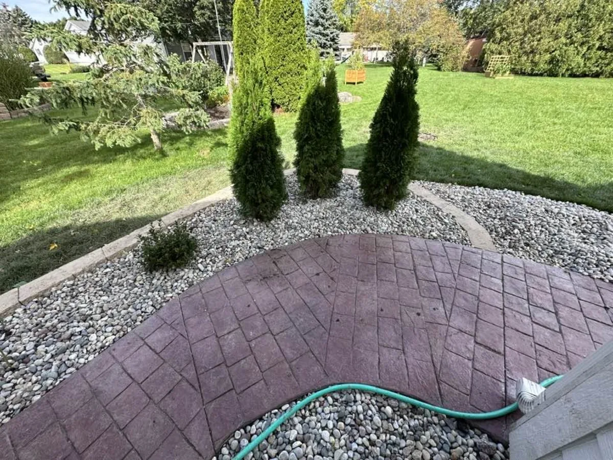 Stamped concrete patio bordered by decorative rock and upright evergreens