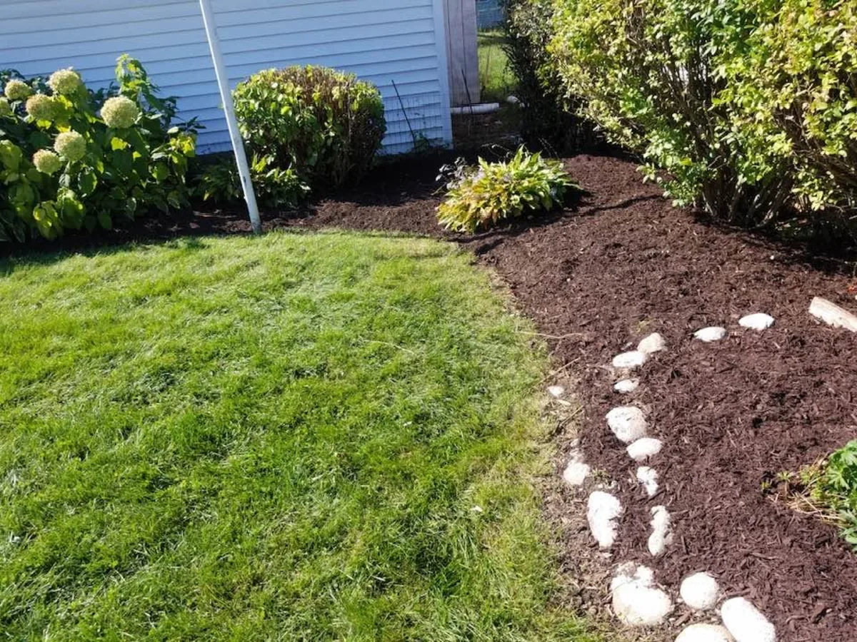 Mulch bed edged with white decorative rock along the side of a house